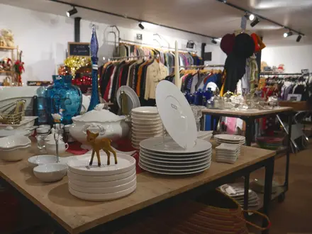 Une table de la boutique garnie de vaisselle blanche, devant les portants de vêtements de la recyclerie.