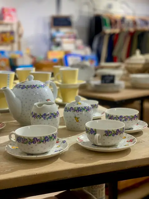 Un service à thé en porcelaine à décor de fruits, posé sur une table de la boutique.