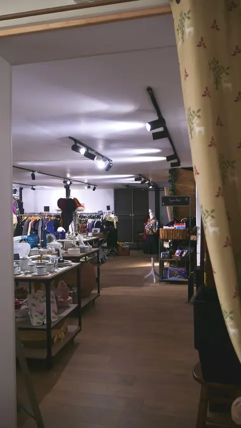 Vue d'ensemble de la boutique : allée centrale, tables de vaisselle et portants de vêtements.