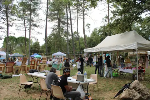 Le stand de La Source et ceux des voisins sous les pins, entre chevalets, guirlandes de fanions et tables de bénévoles.