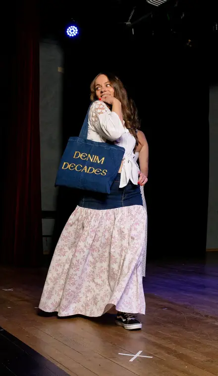 Une mannequin sur la scène du défilé Denim Decades, un tote-bag en jean brodé « Denim Decades » à l'épaule.