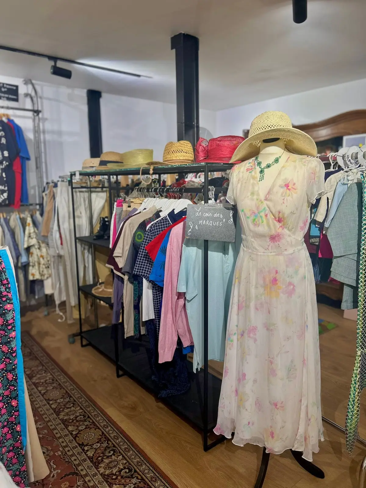 Le coin textile : portants de vêtements, chapeaux de paille et robe fleurie sur mannequin.