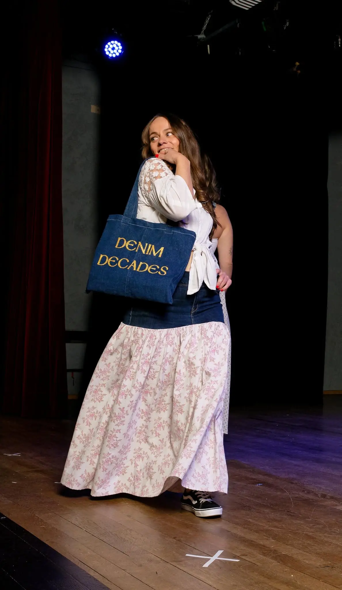 Une mannequin sur la scène du défilé Denim Decades, un tote-bag en jean brodé « Denim Decades » à l'épaule.